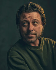 Middle aged man with stubble beard in green sweater.