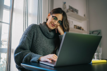Happy young woman sitting at home in earphones using laptop computer having chat online with friends via app, businesswoman working at home having online meeting in video call with colleagues