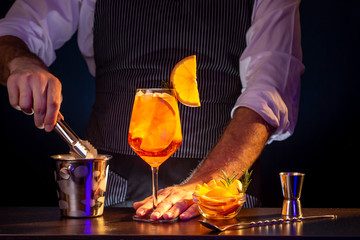 Bartender adding ice from an ice bucket into Aperol spritz cocktail glass