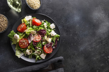 Healthy vegan salad in black dish with fresh tomato, greens, seeds hemp for clean eating. Top view.