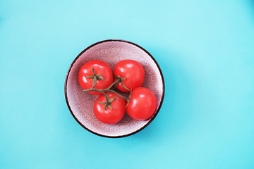 Bright red tomatoes on a blue background in a white plate. Vegetarian lifestyle and healthy food - top view.