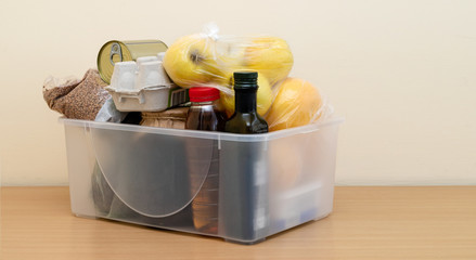 Plastic box with a set of food: eggs, buckwheat, apples, oranges, fruits, oil, canned food. Donation table.