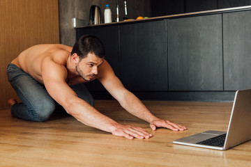 Fototapeta na wymiar muscular man doing balasana exercise while watching online yoga training on laptop