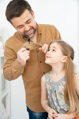dad makes ponytails of her little daughter