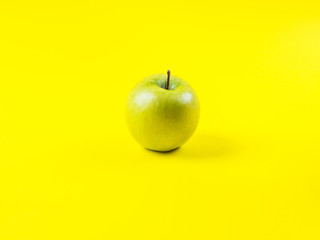 Shiny fresh green apple on bold yellow background. Healthy diet minimal concept. Vitamins