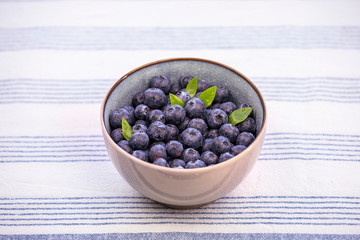 Bowl with blueberries  and green leaves  decoration on the kitchen table with bright striped tablecloth.