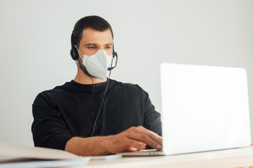 selective focus of operator in medical mask and headset working from home with laptop