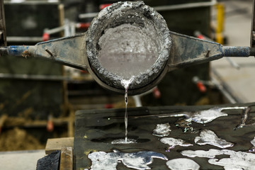 Detail Close up of the metal sand casting technique, pouring molten aluminum silver colored liquid...