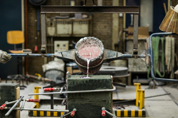 Metal sand casting technique pouring molten aluminum silver colored liquid into a mold in a industrial environment, workshop space