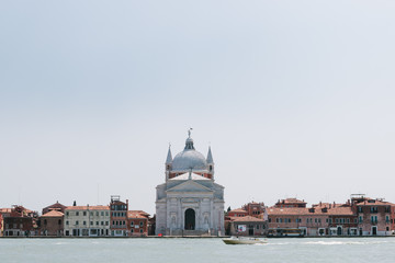 Fototapeta na wymiar Street of Venice in summer time. Italian view. Roof, sea canal in sunny day. Old city, ancient buildings. Italy. Popular tourist destination of Italy. Europe. Church of the savior. Chiesa di Redentore