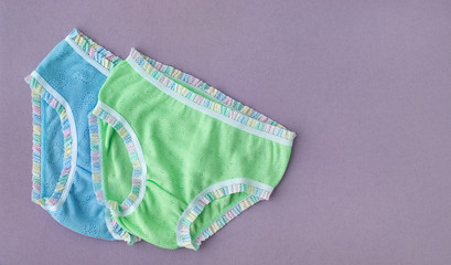 Children's underwear on a lilac background. Clothes for children in the form of underwear. Panties for girls from soft knitwear. There is space for text.