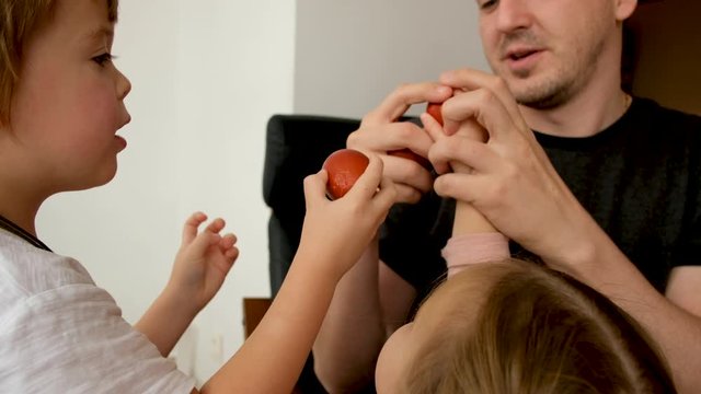 Cheerful adult man smiling and tapping eggs with children while celebrating Easter at home together