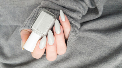 Female hand with long nails and a white gray manicure holds a bottle of nail polish
