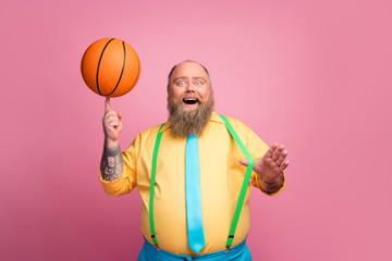 Portrait of his he nice cheerful cheery bearded guy spinning orange ball on finger having fun isolated over pink pastel color background