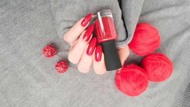 Female hand with long nails and a bottle bright red color nail polish