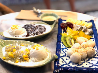 Thai sweet dessert Tapioca pearl pudding with coconut milk green sago in bowl, yellow sweet corn and ice cream in leaf plate eat with fruits, Kiwi, dragon fruit and banana, put in flower blue plate.