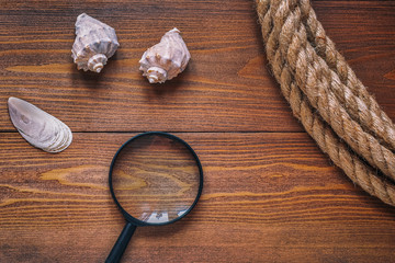 Shells, magnifying glass and rope against dark brown wooden boards as background texture.