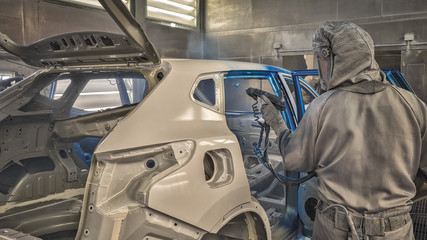 An employee of the car body painting shop paints the interior elements of a car.