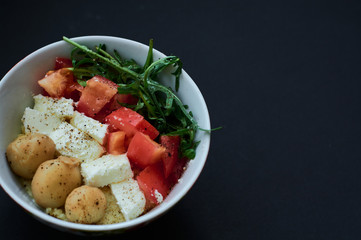 Black background and bowls with healthy, useful kus-kus breakfast with vegetables, tomatoes, mushrooms, arugula and cheese.