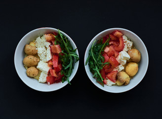 Black background and bowls with healthy, useful kus-kus breakfast with vegetables, tomatoes, mushrooms, arugula and cheese.