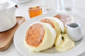 Soft focus on the cups, tea and teapot in the background, and a close-up of pancakes and cream on a white plate