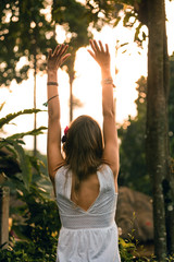 Woman holding hands in the air with orange sunlight in the background.