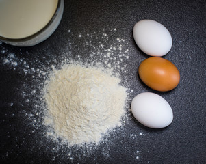 Ingredients for a cake. Eggs, milk, flour on a black background. 