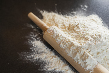 Rolling pin and flour on black table. Wheat flour on a black background.