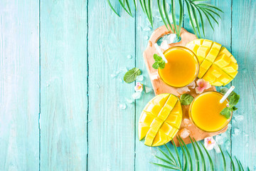 Fresh summer tropical fruit drink. Mango smoothie or mango juice, with fresh mango and tropical leaves on outdoor wooden background. Copy space top view.