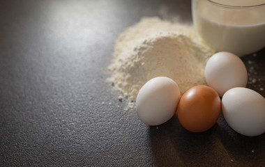 Ingredients for baking on a black background. Ingredients for the dough. Eggs, milk, flour.