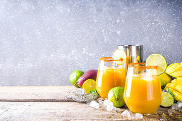 Summer tropic mexican cold cocktail. Mango margarita cocktail, with tequila, lime, lemon, hot chili jalapeno peppers. Wooden background with bar party utensils copy space