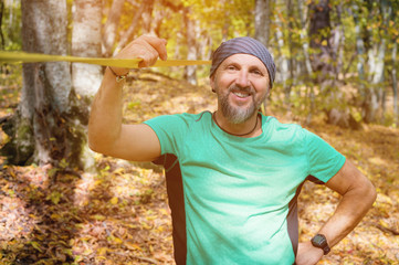 Portrait of a bearded athletic man engaged in slack next to a stretched sling for balance in the autumn forest. Smiling athlete 40 years old on a sunny day