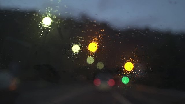 Parabrisas de un coche bajo una tormenta. Llueve y se reflejan las luces de los coches.