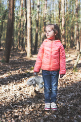 Little girl child standing on stump in a forest during a walk on sunny spring day keeping a toy teddy bear looking away