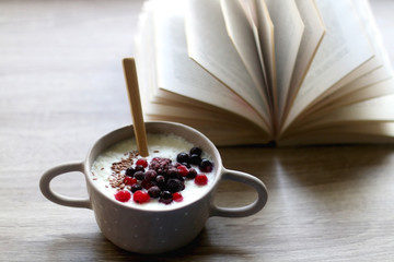 Bowl of rice porridge with berries and open book. Selective focus.