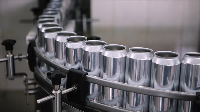 Technological line for bottling of beer in brewery. Empty aluminum beer cans are moving along the conveyor belt. Clean beer bottles are moving along the conveyor.Industry, production line, close up.