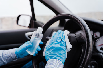 unrecognizable man in a car using alcohol gel to disinfect steering wheel during pandemic...