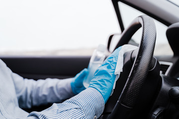 unrecognizable man in a car using alcohol gel to disinfect steering wheel during pandemic...