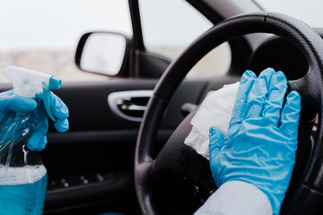 unrecognizable man in a car using alcohol gel to disinfect steering wheel during pandemic coronavirus covid-19