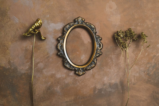 Empty vintage oval photo frame and twigs of dried flowers on decorative brown backdrop.