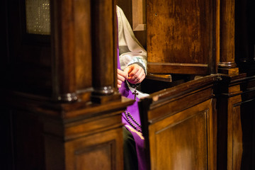 priest in the confessional recites the rosary awaiting penitent - obrazy, fototapety, plakaty