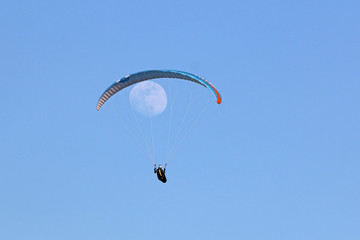 Paraglider flying wing in a blue sky with the moon	