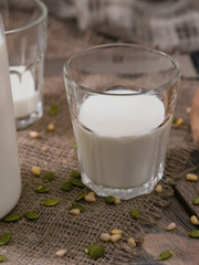 Glass and jug with milk and scattered seeds and nuts on wooden table. Country breakfast on World Milk Day.