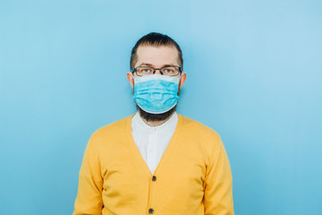 A young man in a medical mask on a blue background. A man in a yellow cardigan shows a hand gesture OK. We're going to beat coronavirus. The COVID-2019 epidemic. Positive boy.