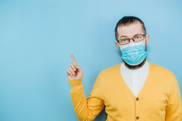 A young man in a medical mask on a blue background. A man in a yellow cardigan shows a hand gesture OK. We're going to beat coronavirus. The COVID-2019 epidemic. Positive boy.