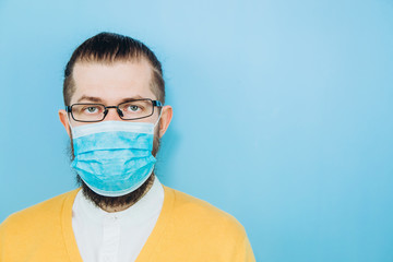 A young man in a medical mask on a blue background. A man in a yellow cardigan shows a hand gesture OK. We're going to beat coronavirus. The COVID-2019 epidemic. Positive boy.