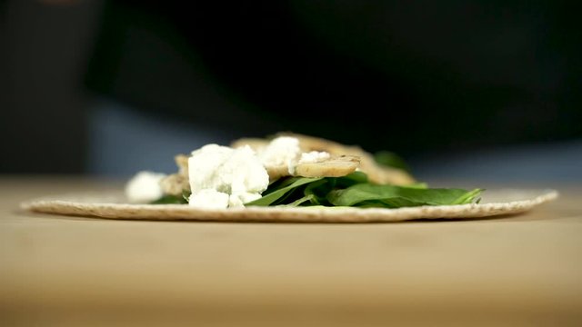 Las manos de una chica joven ponen queso feta sobre un wrap de espinacas.