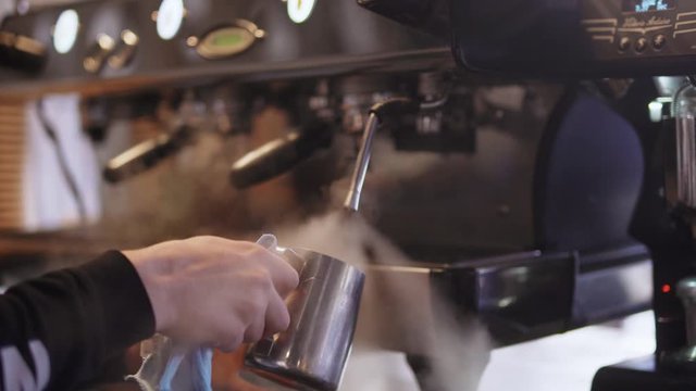 Barista wipes the metal milkman after making coffee by the coffee machine