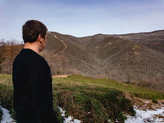 A man stands near green tea bushes against the backdrop of the mountains. The most northern tea in the mountains of the Caucasus.