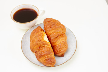 Two croissants on a white plate and a cup of black coffee on white table. Selective focus